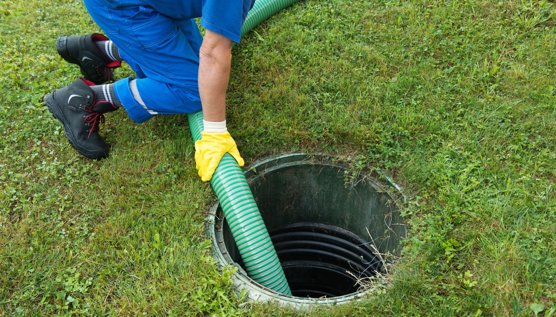 A technician in yellow gloves is feeding a green pumping hose down into the septic tank riser for affordable septic tank cleaning in Langley.